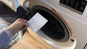 hand steekt wasstrip in de wasmachine
